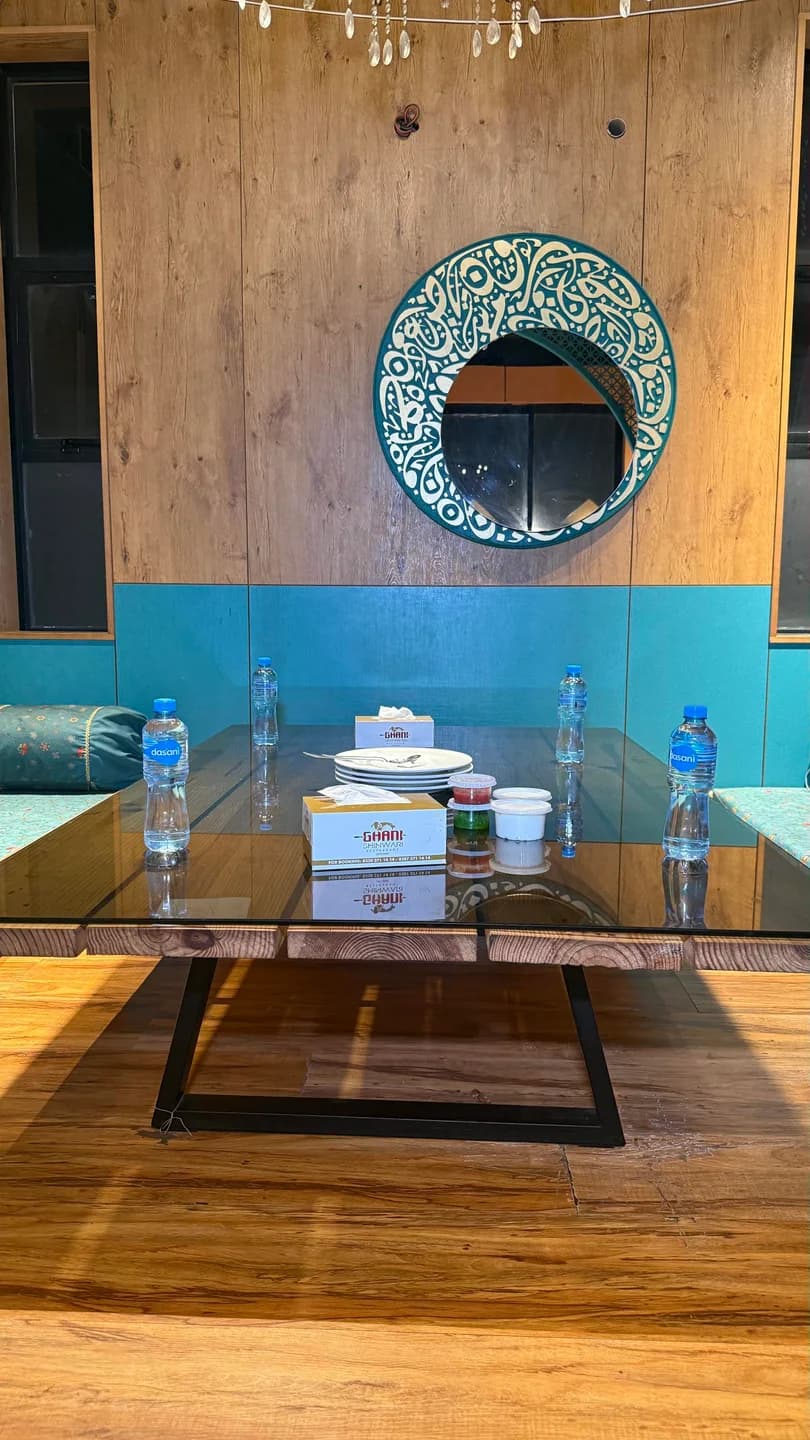 Low wooden dining table surrounded by floor cushions, with turquoise panels and a decorative round mirror