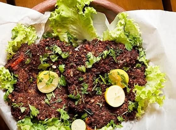 A chapli kabab serving with lemon and herbs; the meat variant is not specified in the photograph